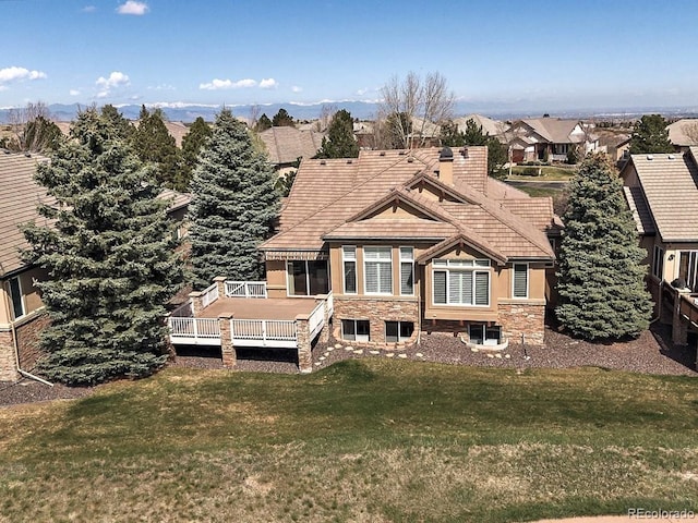back of property featuring a wooden deck, a chimney, a yard, and stone siding