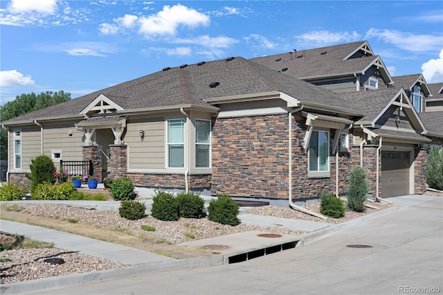 view of front of home with a garage, stone siding, roof with shingles, and concrete driveway