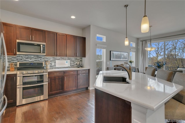 kitchen featuring decorative light fixtures, a breakfast bar area, stainless steel appliances, a kitchen island with sink, and a sink