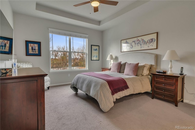 bedroom with baseboards, a raised ceiling, and light colored carpet