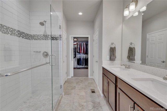 bathroom featuring double vanity, a shower stall, a walk in closet, and a sink