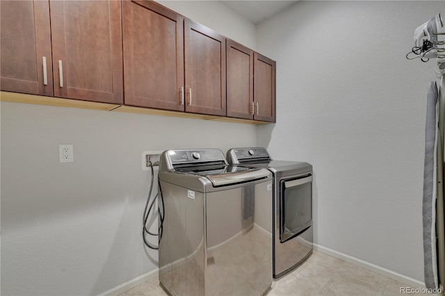 washroom featuring cabinet space, washing machine and dryer, light tile patterned floors, and baseboards