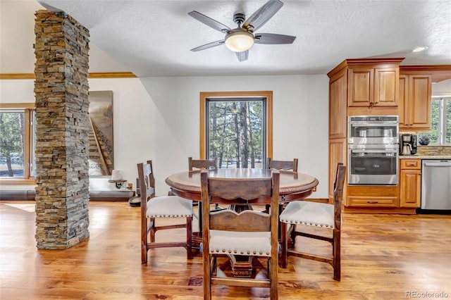 dining room featuring ceiling fan, light hardwood / wood-style flooring, a textured ceiling, and ornate columns