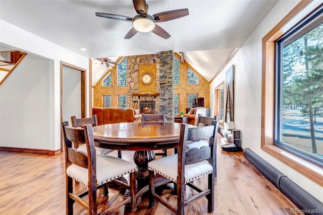 dining space featuring lofted ceiling, a stone fireplace, ceiling fan, and light hardwood / wood-style flooring