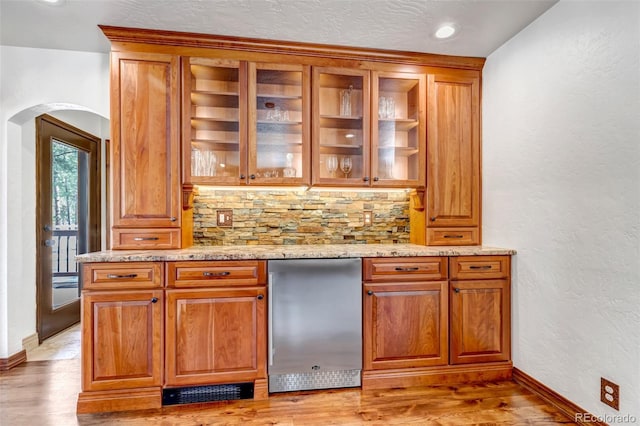 bar featuring tasteful backsplash, light stone countertops, refrigerator, and light hardwood / wood-style floors