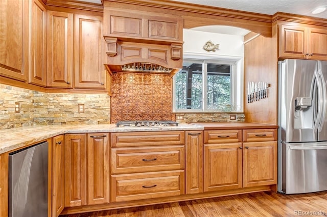 kitchen with tasteful backsplash, appliances with stainless steel finishes, light wood-type flooring, and light stone counters