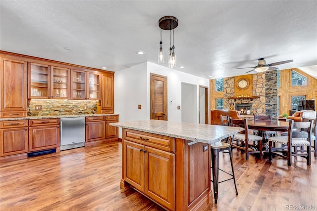 kitchen with hanging light fixtures, a stone fireplace, light stone counters, and light wood-type flooring