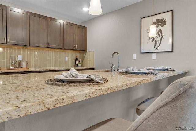 1721 Wingfeather Ln, Castle Rock, CO 80108 - kitchen with backsplash, a breakfast bar area, light stone countertops, pendant lighting, and dark brown cabinets