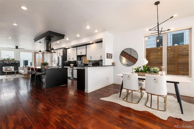 kitchen with dark wood-type flooring, ventilation hood, ceiling fan with notable chandelier, hanging light fixtures, and kitchen peninsula