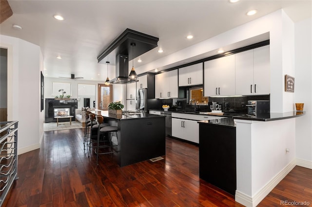 kitchen with island exhaust hood, a kitchen bar, stainless steel appliances, decorative light fixtures, and a kitchen island