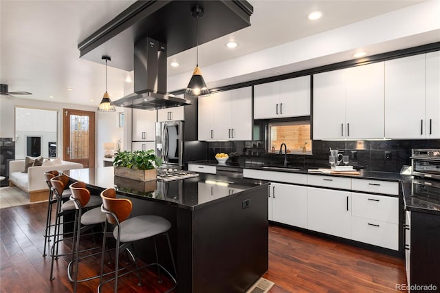 kitchen with a center island, a kitchen breakfast bar, stainless steel refrigerator with ice dispenser, decorative light fixtures, and island exhaust hood