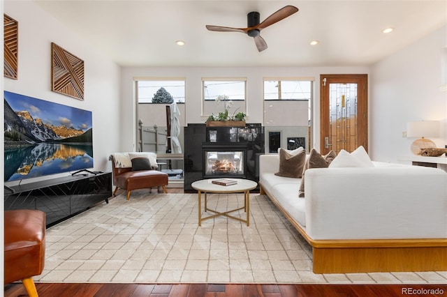 living room with a multi sided fireplace, ceiling fan, and wood-type flooring