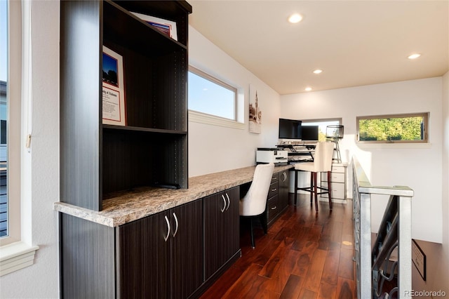 kitchen with a kitchen bar, dark brown cabinets, built in desk, and dark hardwood / wood-style floors