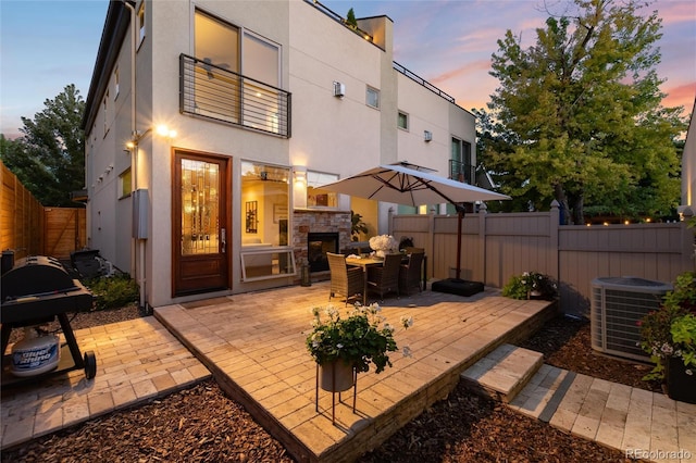 back house at dusk with an outdoor stone fireplace, a patio, and central AC