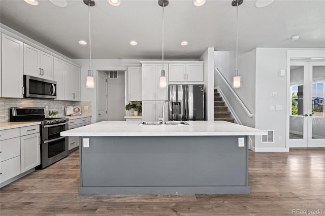 17970 E 106th Pl, Commerce City, CO 80022 - kitchen featuring appliances with stainless steel finishes, french doors, wood finished floors, an island with sink, and tasteful backsplash
