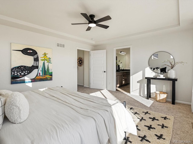 bedroom featuring light colored carpet, visible vents, baseboards, a tray ceiling, and ensuite bath