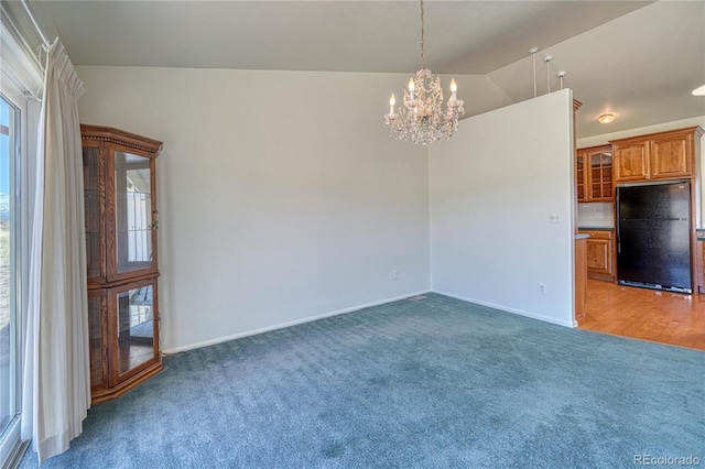 empty room with a notable chandelier, a healthy amount of sunlight, vaulted ceiling, and dark colored carpet