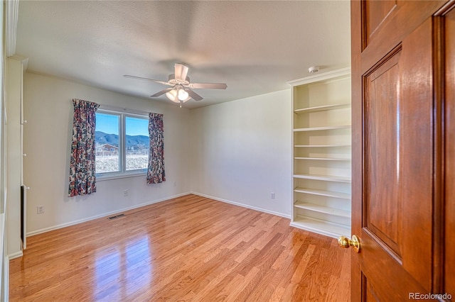 unfurnished room featuring ceiling fan, a mountain view, a textured ceiling, and light hardwood / wood-style floors