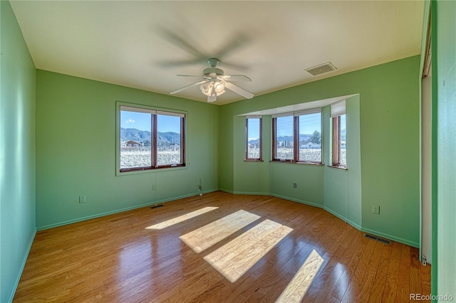 unfurnished room with a mountain view, ceiling fan, and light hardwood / wood-style flooring