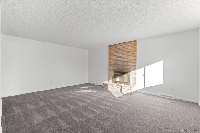 unfurnished living room with dark colored carpet, a textured ceiling, and a brick fireplace