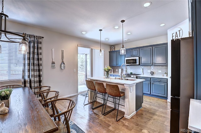 kitchen with light wood-type flooring, a breakfast bar, stainless steel appliances, light countertops, and decorative backsplash