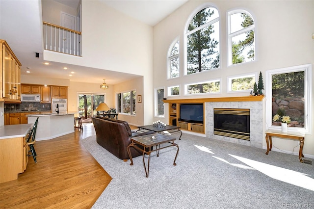 living area featuring baseboards, a tiled fireplace, light wood-type flooring, recessed lighting, and a high ceiling