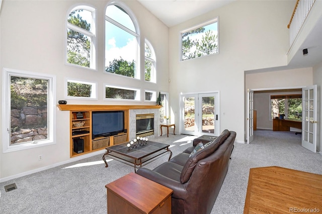 carpeted living room featuring visible vents, a tiled fireplace, french doors, a high ceiling, and baseboards