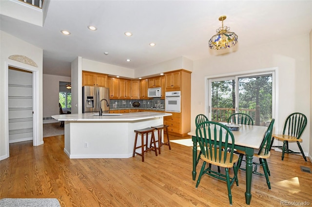 kitchen with backsplash, an island with sink, light wood-style flooring, white appliances, and a sink