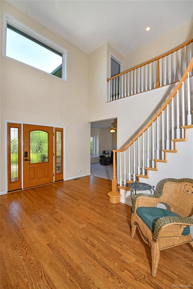 entrance foyer featuring a towering ceiling, baseboards, wood finished floors, and stairs