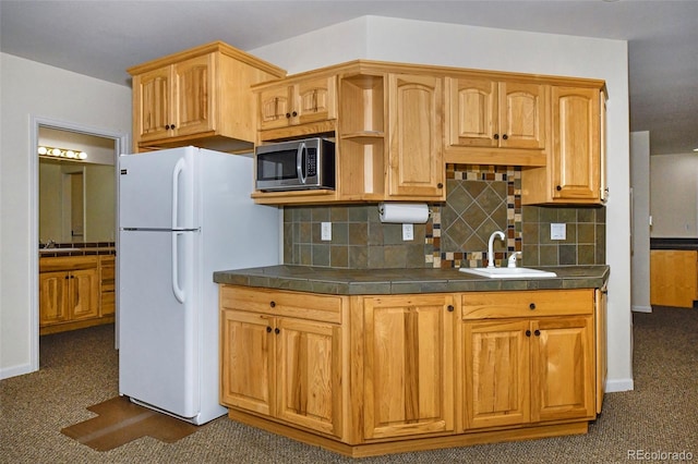 kitchen featuring a sink, stainless steel microwave, dark countertops, freestanding refrigerator, and decorative backsplash