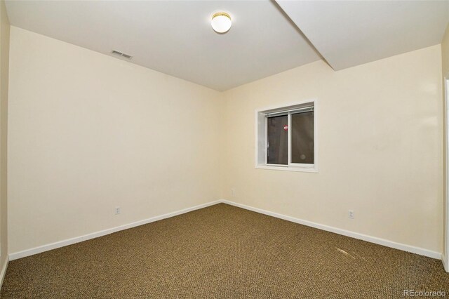 spare room featuring dark colored carpet, visible vents, and baseboards