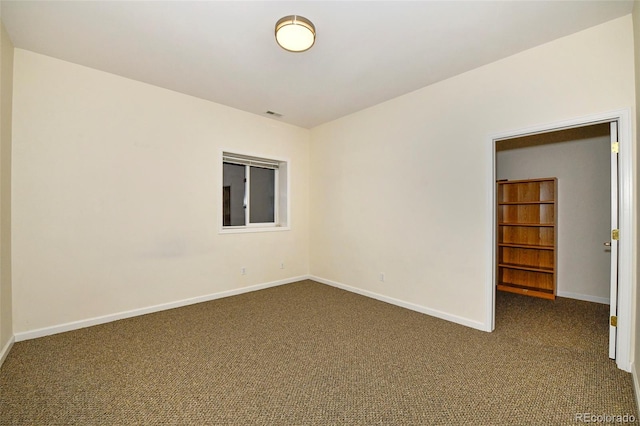 spare room with baseboards and dark carpet