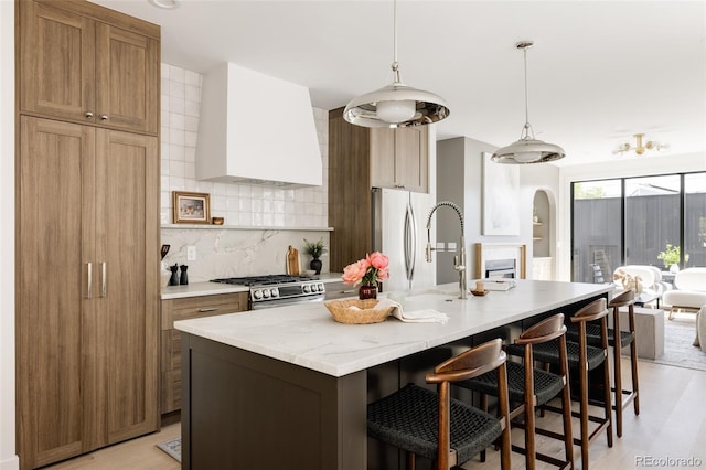 3932 Kalamath St, Denver, CO 80211 - kitchen featuring stainless steel appliances, wall chimney range hood, decorative backsplash, arched walkways, and an island with sink