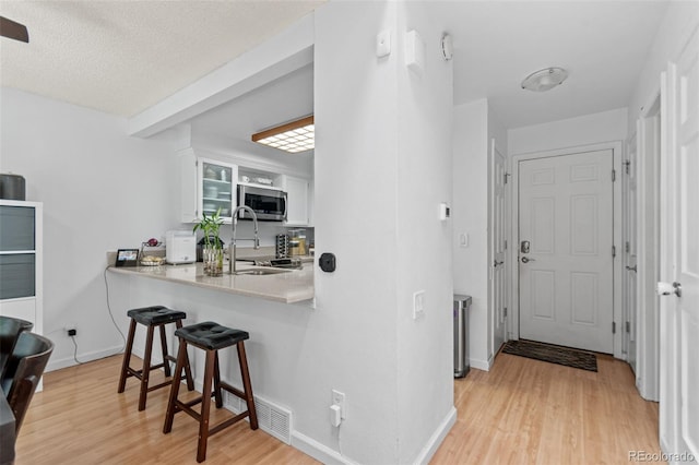 2092 S Helena St Unit C, Aurora, CO 80013 - kitchen featuring stainless steel microwave, a breakfast bar area, light wood-style flooring, white cabinets, and light countertops