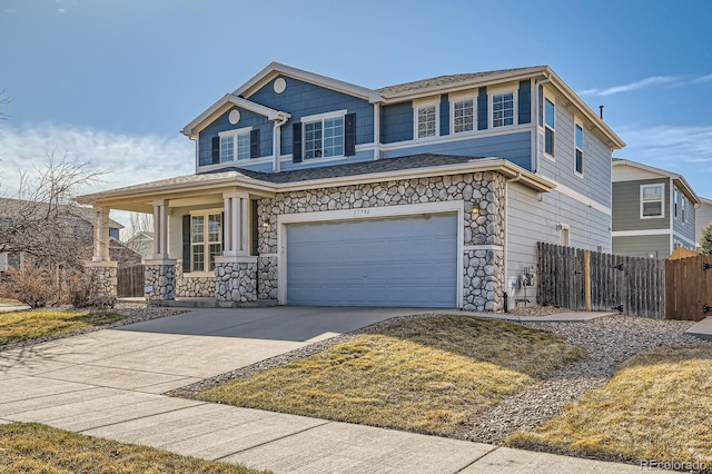 view of front facade featuring fence, driveway, an attached garage, covered porch, and stone siding