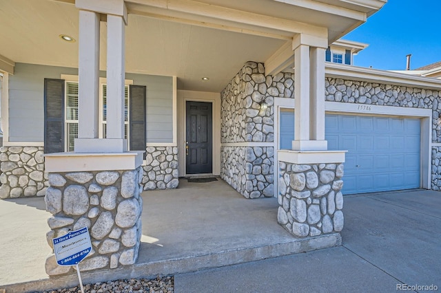 entrance to property with stone siding, a porch, driveway, and a garage