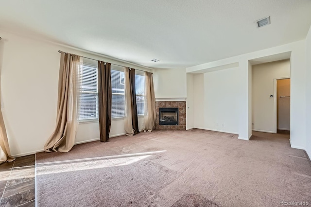 unfurnished living room with visible vents, baseboards, carpet floors, and a tiled fireplace