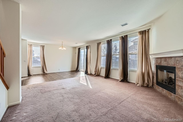 unfurnished living room featuring visible vents, an inviting chandelier, carpet flooring, baseboards, and a tile fireplace