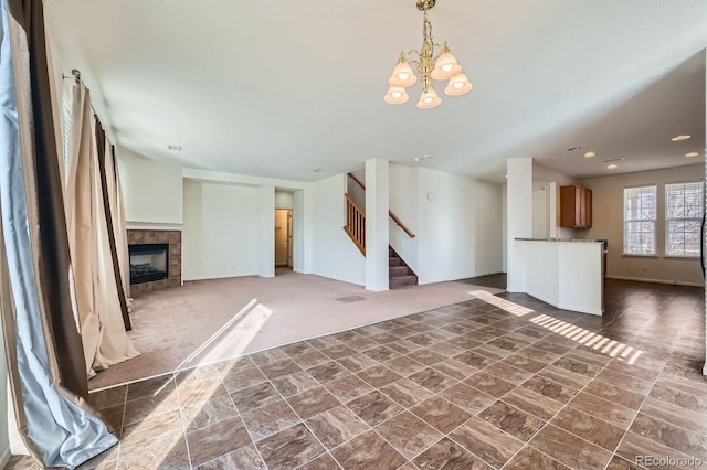 unfurnished living room featuring a tiled fireplace, dark carpet, recessed lighting, a chandelier, and stairs