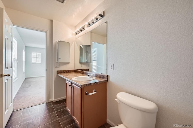 half bath featuring vanity, toilet, a textured wall, and baseboards