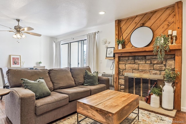 living room with ceiling fan, wood-type flooring, a stone fireplace, and a wall mounted air conditioner