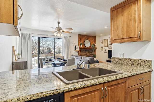 kitchen featuring sink, dishwasher, ceiling fan, light stone countertops, and a textured ceiling