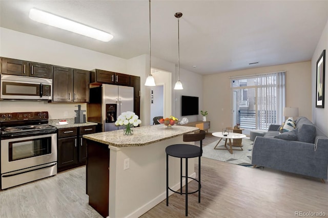 kitchen with a center island, stainless steel appliances, light hardwood / wood-style flooring, decorative light fixtures, and a breakfast bar area