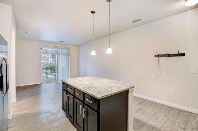 kitchen featuring stainless steel fridge with ice dispenser, light stone counters, light hardwood / wood-style flooring, decorative light fixtures, and a kitchen island