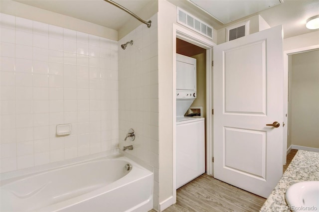 bathroom with vanity, tiled shower / bath combo, stacked washer and clothes dryer, and hardwood / wood-style flooring