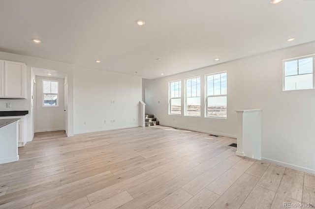 unfurnished living room featuring stairs, recessed lighting, baseboards, and light wood finished floors