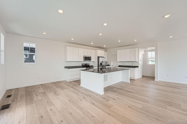 kitchen with dark countertops, visible vents, a center island with sink, light wood-type flooring, and appliances with stainless steel finishes