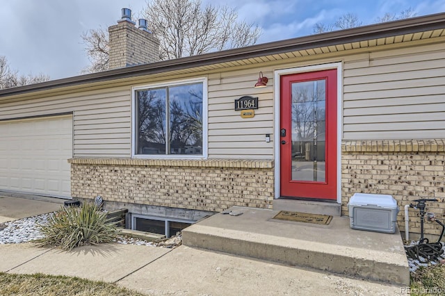 view of exterior entry featuring brick siding, a chimney, and an attached garage