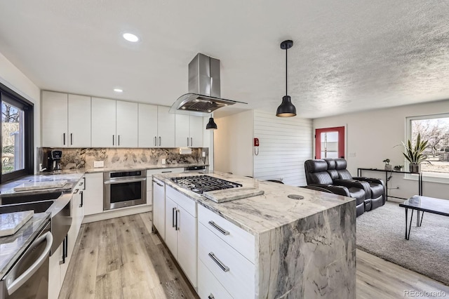 kitchen with stainless steel appliances, light wood-style floors, backsplash, and island range hood