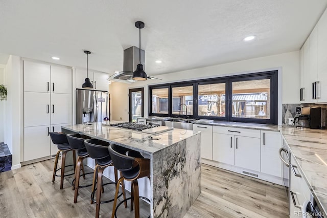 kitchen with stainless steel appliances, a sink, island range hood, and light stone countertops